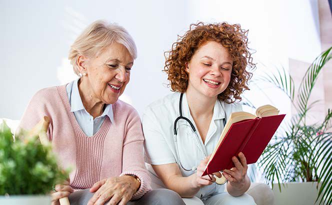 Eine Pflegerin liest einer älteren Dame etwas aus einem Buch vor.