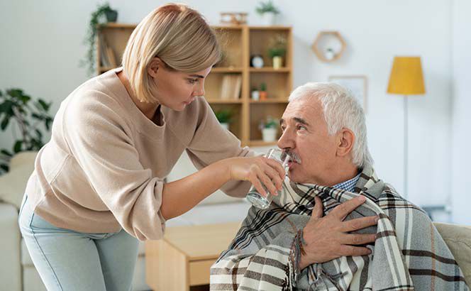 Eine Pflegerin hilft einem älteren Herren beim Trinken.