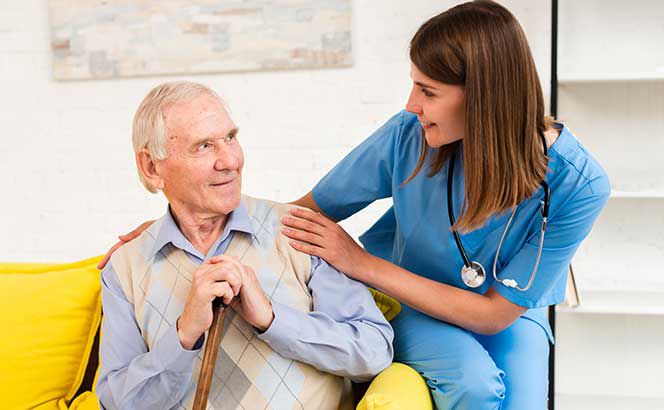 Eine Pflegerin im Gespräch mit einem älteren Herren, ihre Hände berühren dabei seine Schultern.